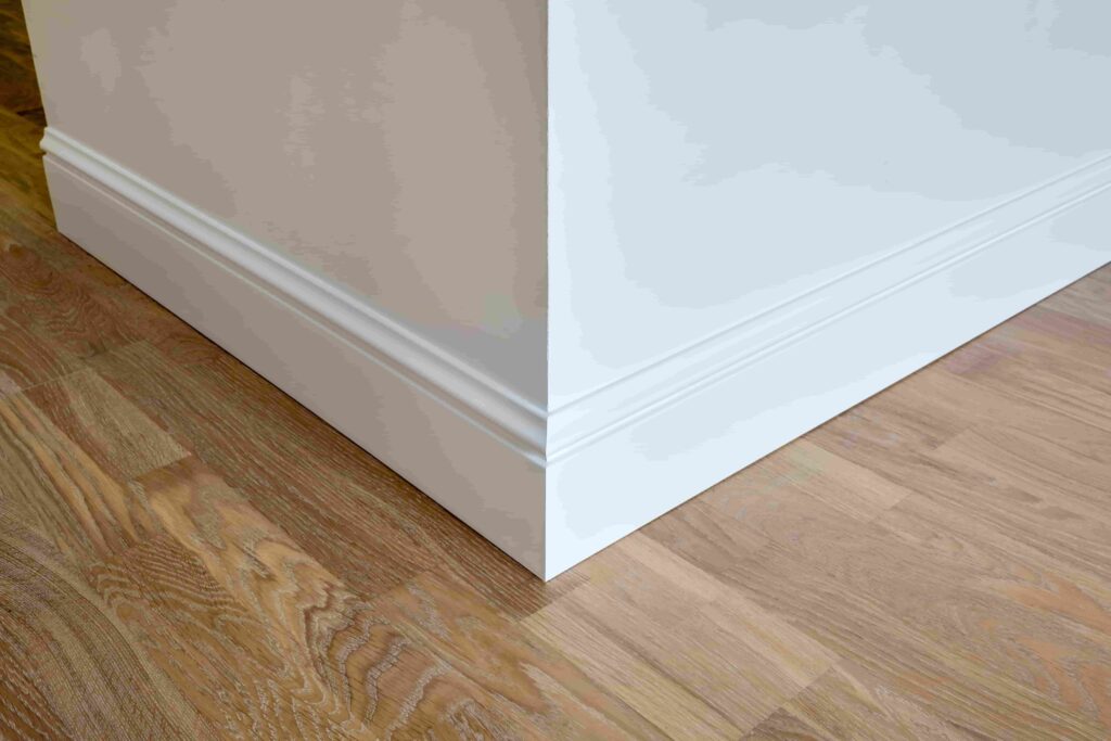 Eine Holzsockelleiste an der Ecke einer weißen Wand in einem Raum mit Parkettboden.