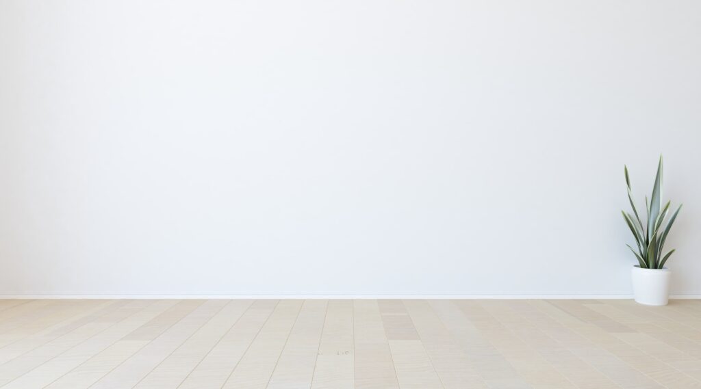 Eine weiße Wand mit weißen Sockelleisten in einem Raum mit Parkettboden.