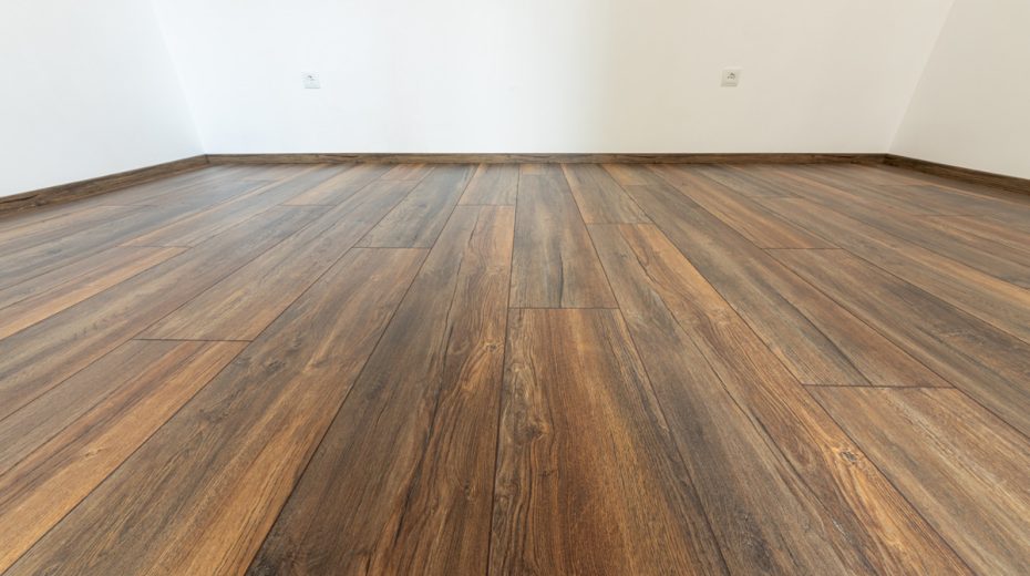 Ein dunkelbrauner Laminatboden in Holzoptik mit passend dazu gewählten dunkelbraunen Sockelleisten entlang der Wand.