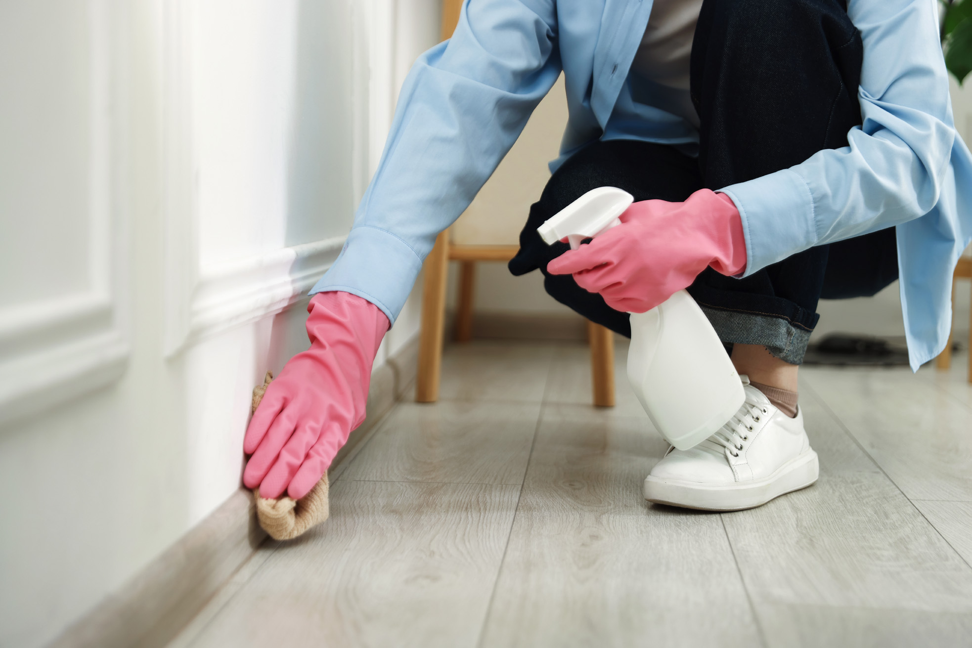 Frau mit Putzhandschuhen und Reinigungsmittel in Sprühdose beim Sockelleisten reinigen